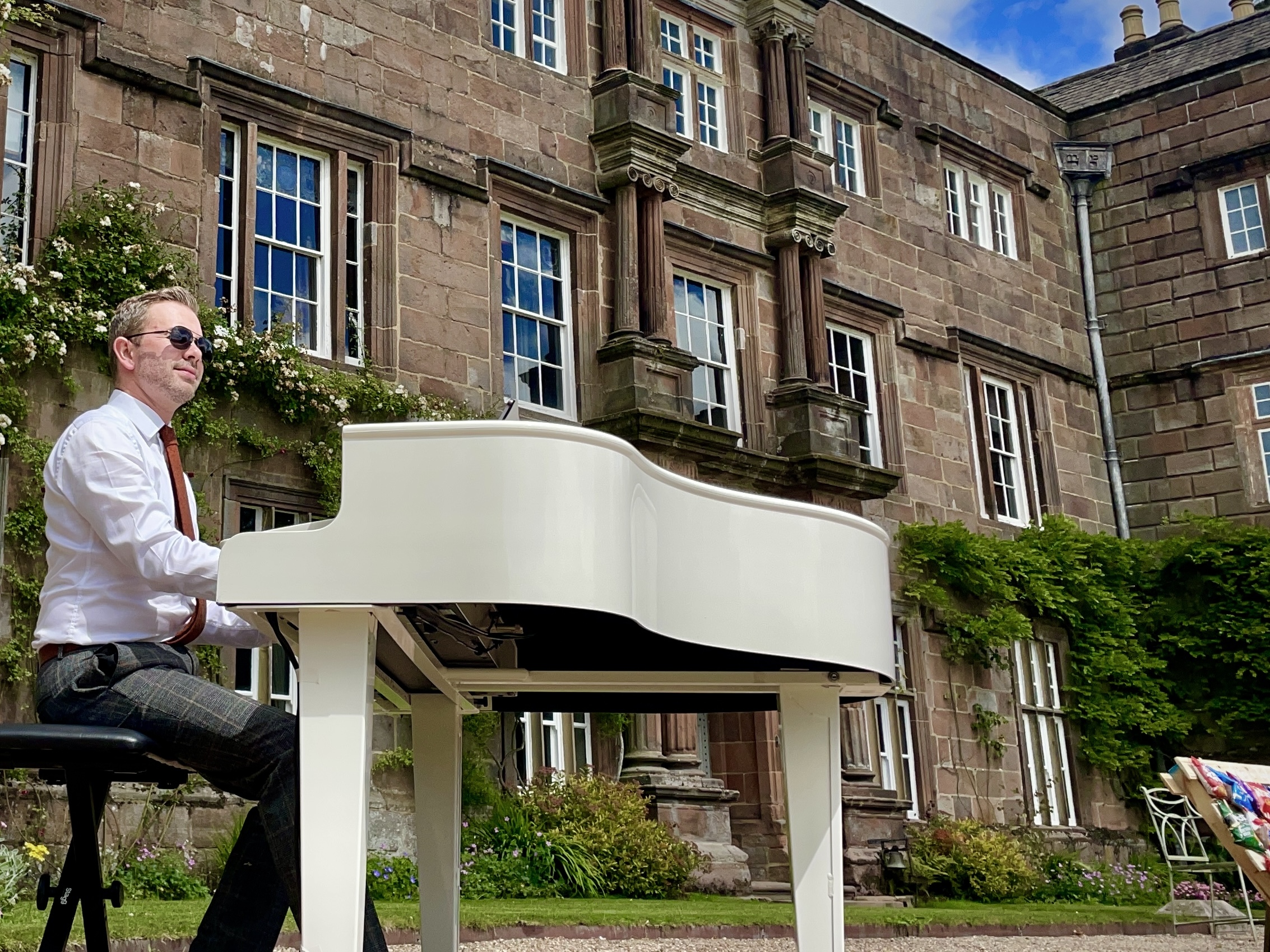 Wedding pianist Craig Smith playing his white piano during an outdoor Browsholme Hall wedding ceremony